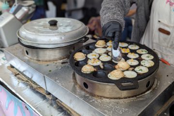 Close-up of a vendor preparing Thai Khanom Krok pancakes at an outdoor market in Leipzig.