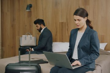 Two business professionals working on laptops in a hotel room, showcasing modern travel lifestyle.