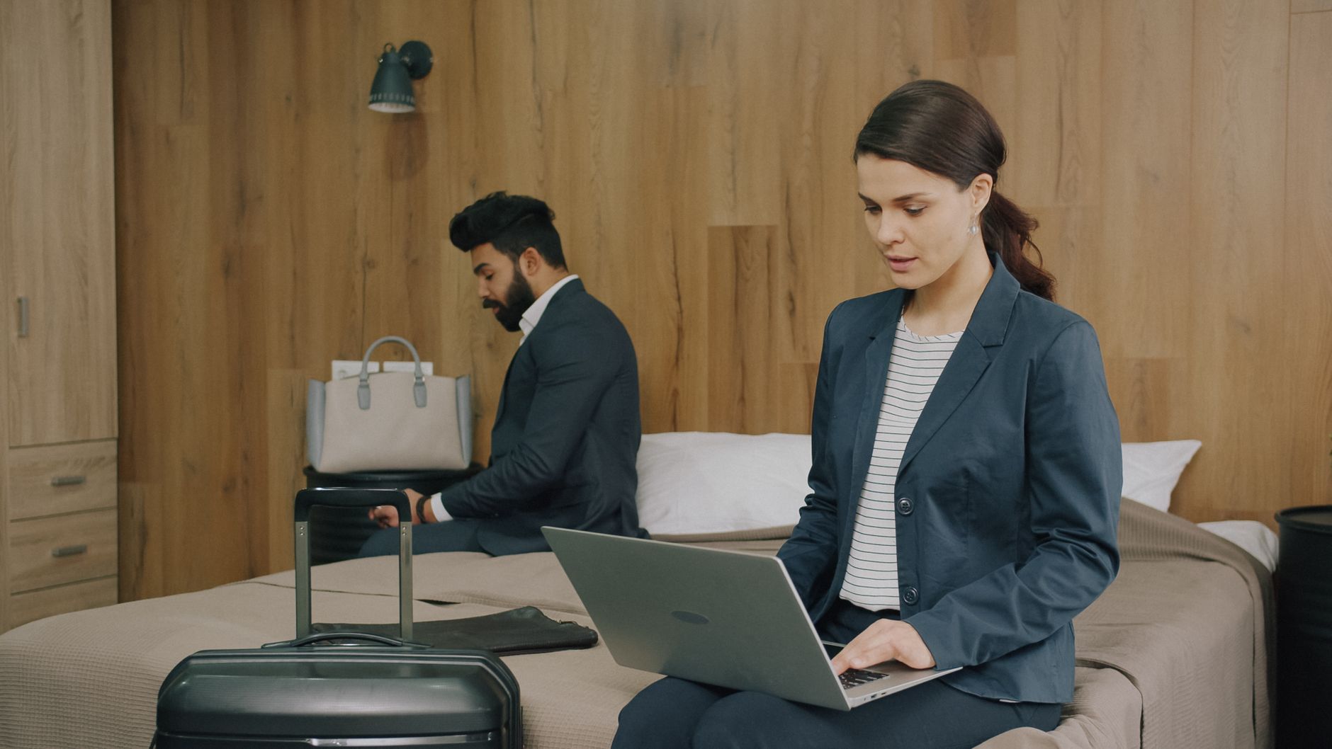 Two business professionals working on laptops in a hotel room, showcasing modern travel lifestyle.