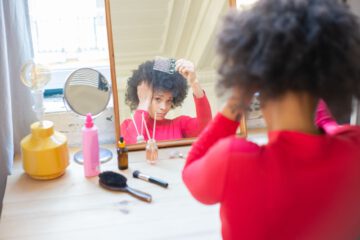 African American woman combing hair in front of a mirror indoors.