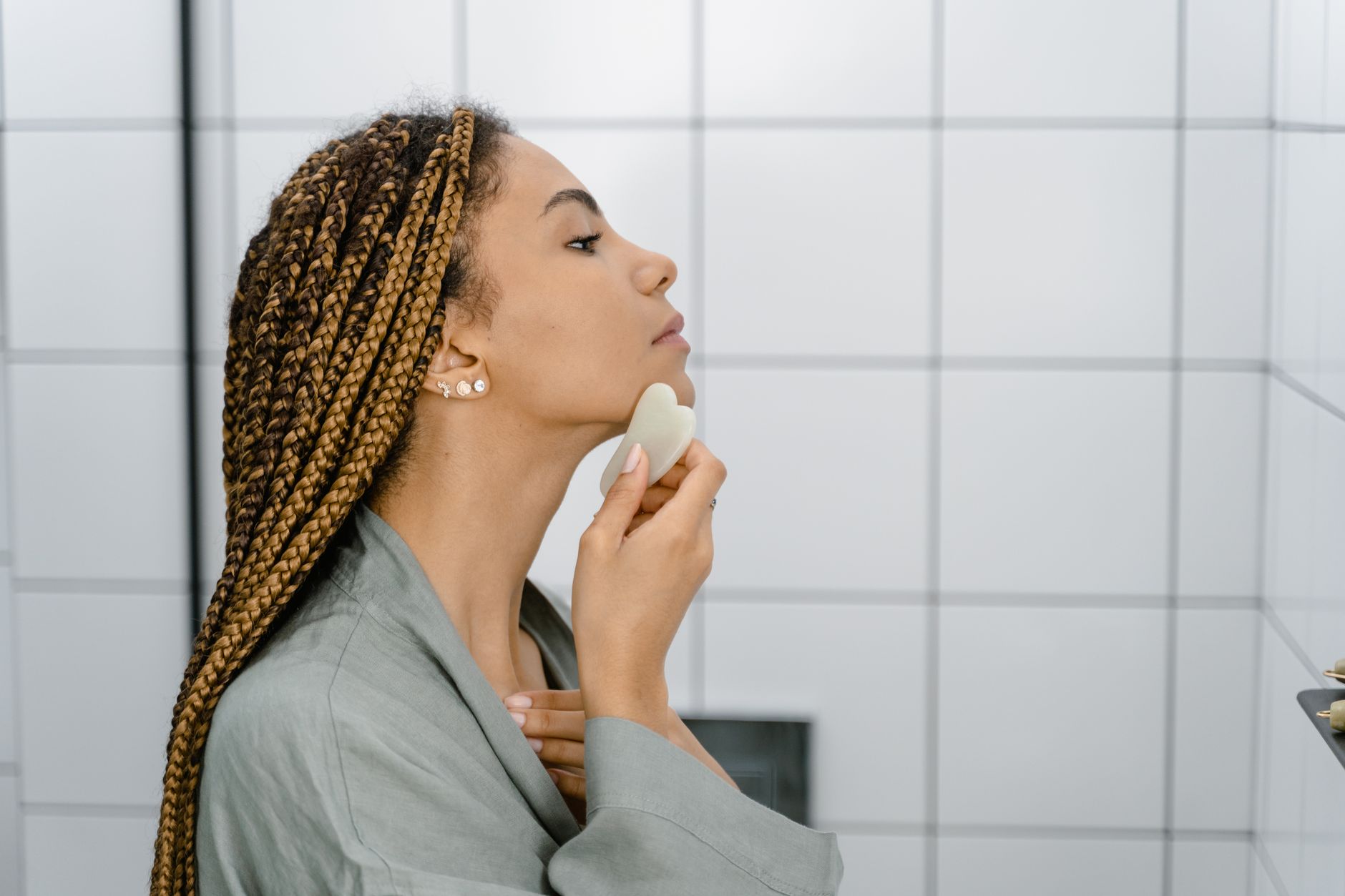 A woman in a bathroom using a gua sha stone for a facial massage routine.