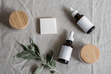 Top view of skincare products with a natural theme, featuring bottles, jars, and a plant on linen cloth.